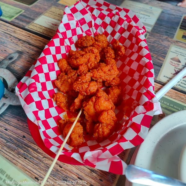 Rib City's boneless BBQ chicken bites in a red and white checkered paper basket on a wooden table.
