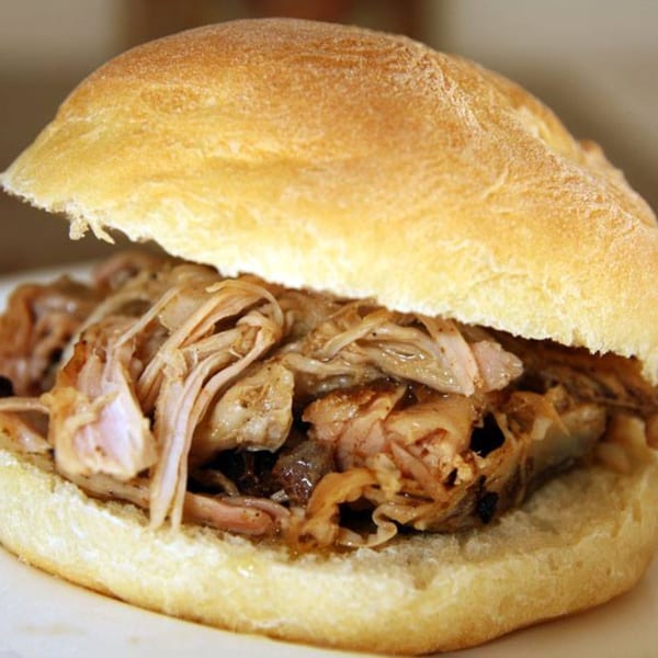 Close-up of a Rib City pulled pork sandwich on a white bun, overflowing with meat.