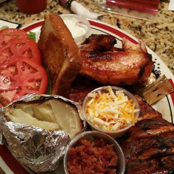 Rib City BBQ plate with grilled chicken, ribs, baked potato, Texas toast, and sides.