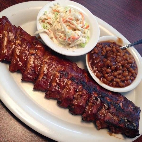 Rib City's full rack of BBQ ribs with sides of coleslaw and baked beans on a white plate.